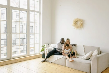 Multiracial family enjoying a cozy reading moment on a modern sofa in a bright living room.