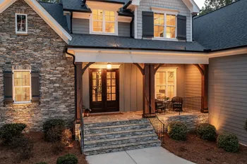 Inviting front porch of a cozy house with stone facade and warm lighting at dusk.