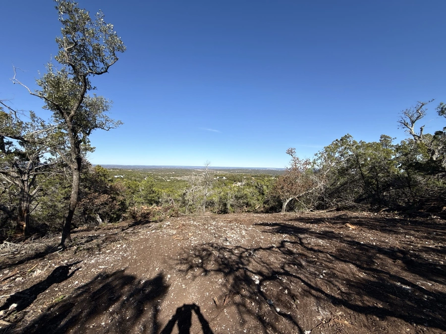 An image showing a rugged, rocky dirt path winding through a lush, wooded landscape with a view of the distant horizon. The scene evokes the natural beauty and remote, untamed character of the Texas Hill Country, highlighting the type of outdoor terrain and environment where A.M. Pitts Construction excels in providing expert land improvement, site preparation, and utility services.