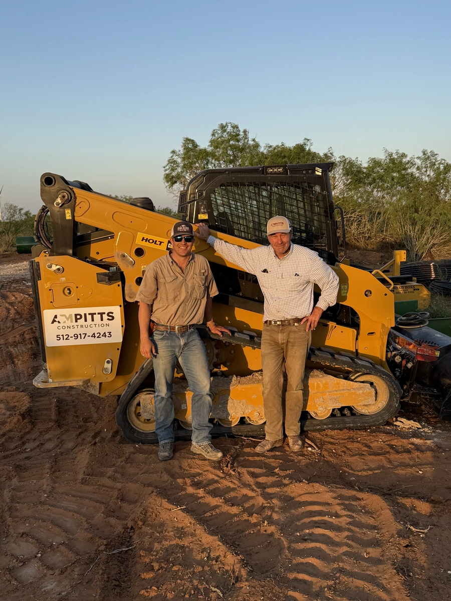 Mason Pitts and his father standing beside a compact track loader at a job site