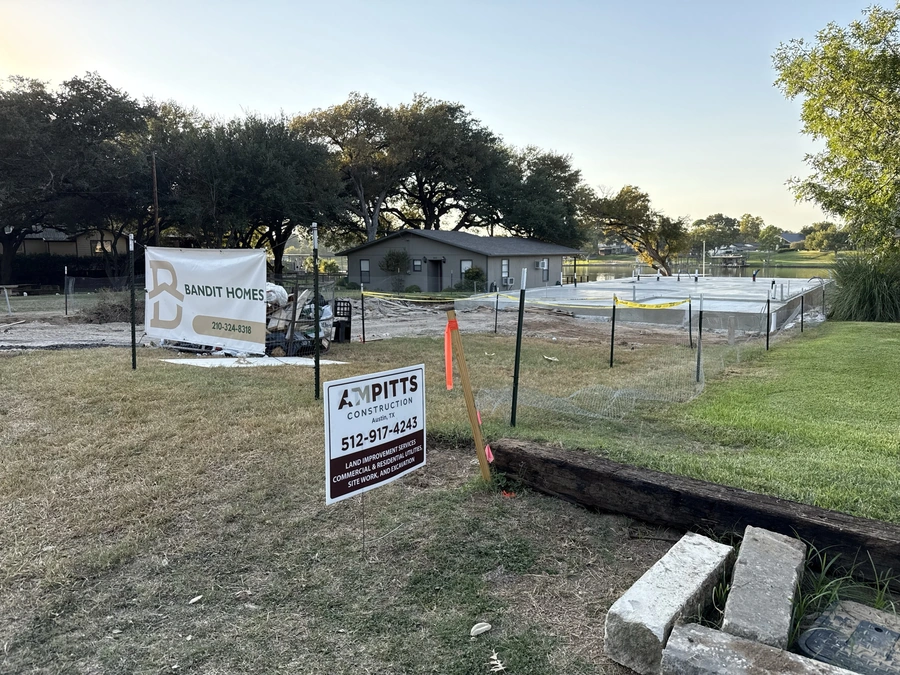 An image showing a construction site for a new housing development. In the foreground, there is a sign for "Bandit Homes" and another sign for "A.M. Pitts Construction" advertising their land improvement, excavation, and utility services. There are trees in the background and a body of water, indicating a scenic, natural setting for the new homes.