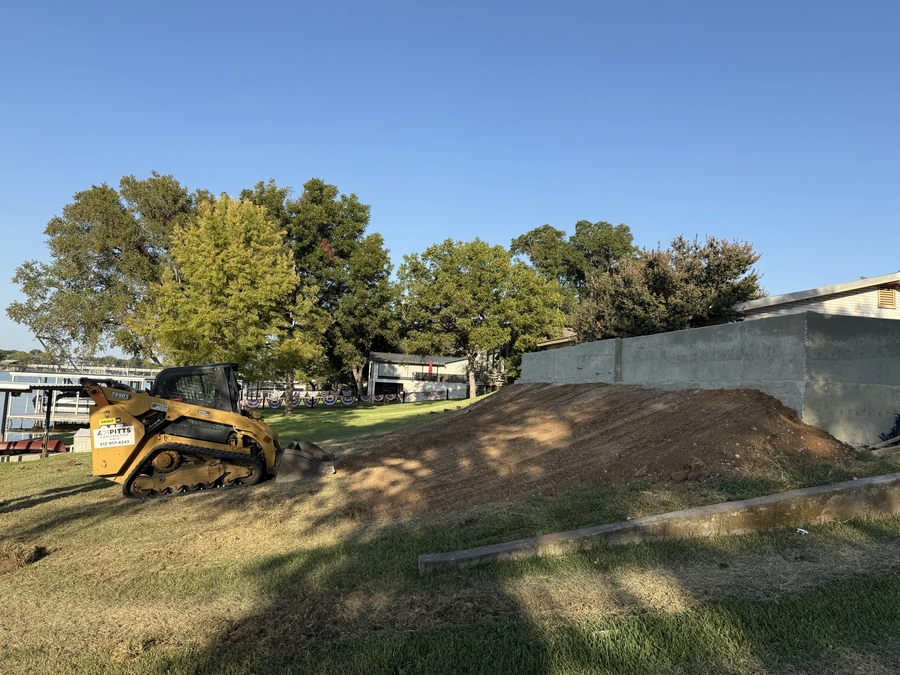 An excavator working on a construction site with piles of dirt and trees in the background.
