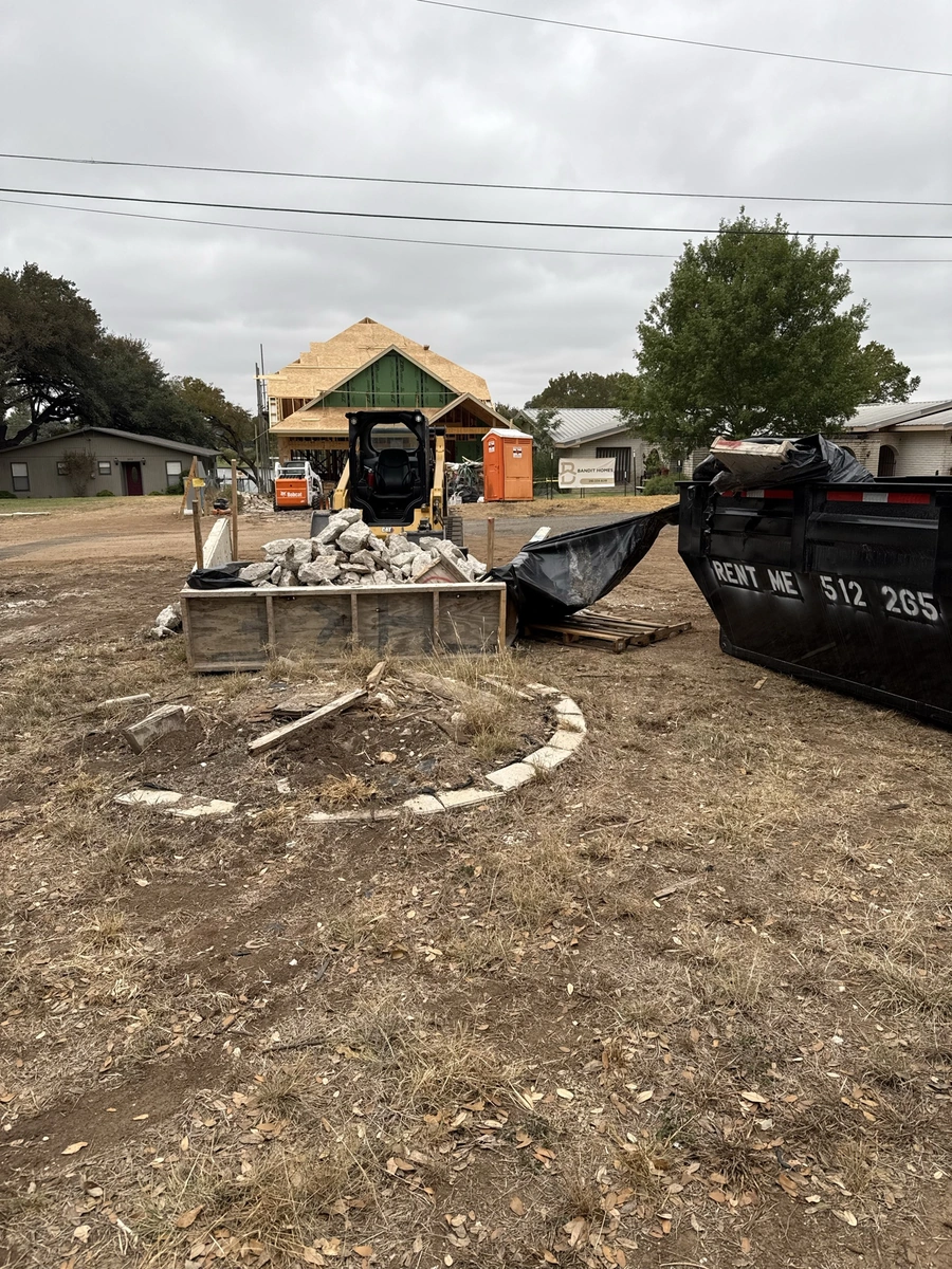 A construction site with a building frame under construction, construction equipment, and debris piles. The scene depicts an active construction project in a rural or semi-rural setting.