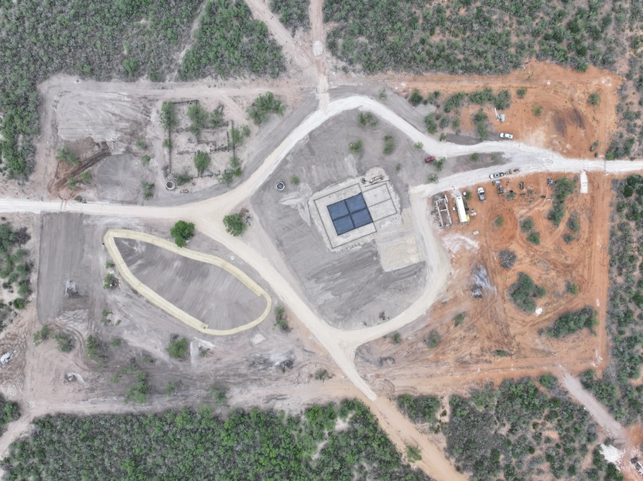 Aerial view of a construction site with a large building, heavy machinery, and dirt roads winding through a forested area.