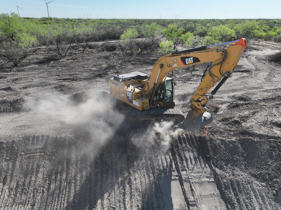 A yellow Caterpillar excavator at work on a construction site, digging up dirt and creating a large dust cloud as it operates.