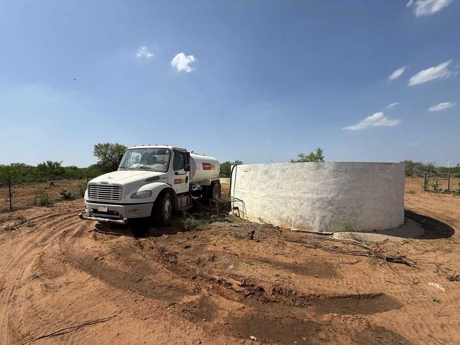 A large concrete water tank or cistern being installed on a rural construction site, with a white utility truck parked next to it.
