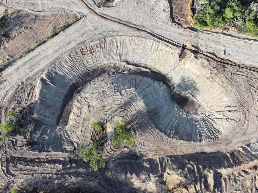 Aerial view of a large open-pit mining operation or quarry, with steep, layered rock walls and heavy equipment operating on the site.