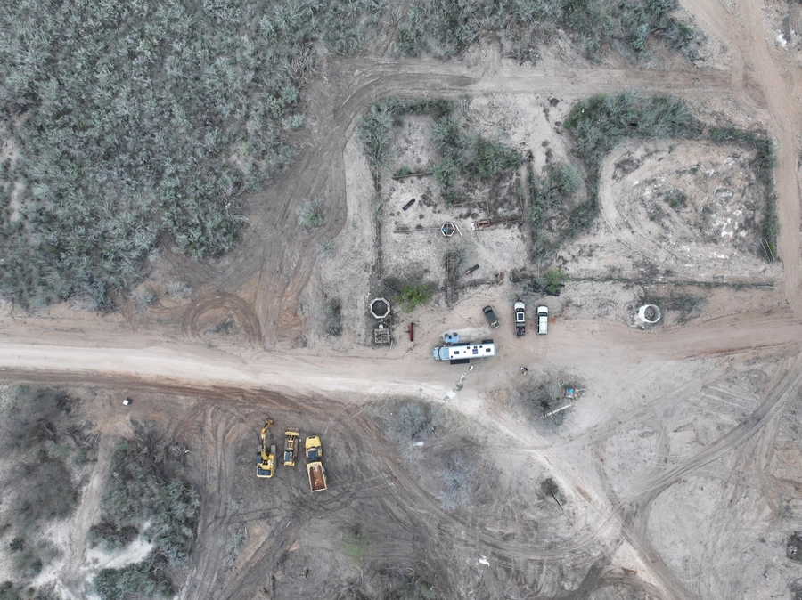 Aerial view of a construction site with heavy machinery, trucks, and temporary structures in a rural, wooded area.