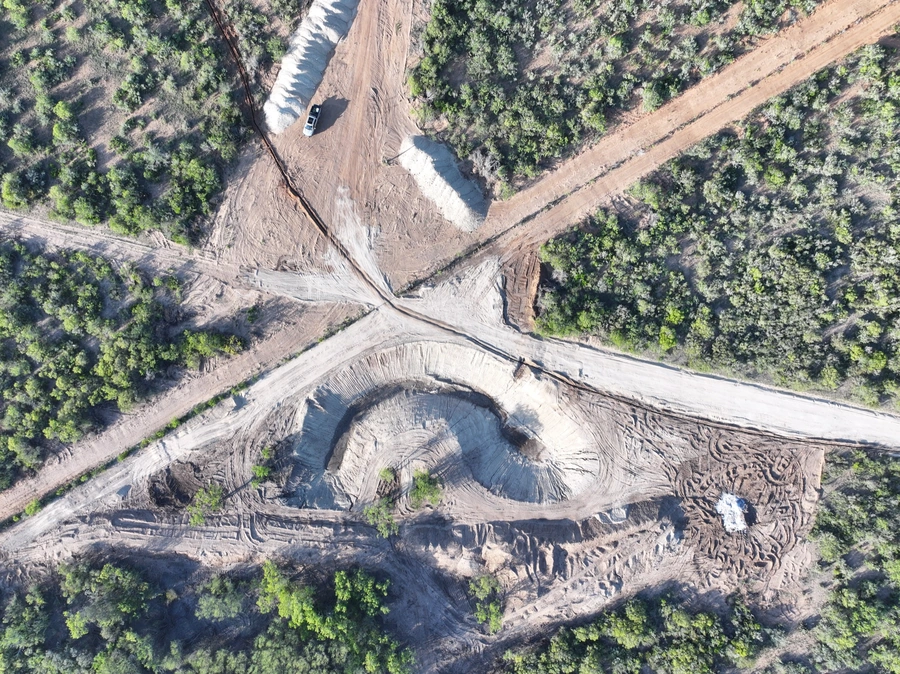 Aerial view of a large-scale excavation and construction site surrounded by dense forestry. Heavy machinery and equipment can be seen operating on the site, which appears to be undergoing significant earthmoving and land development work.