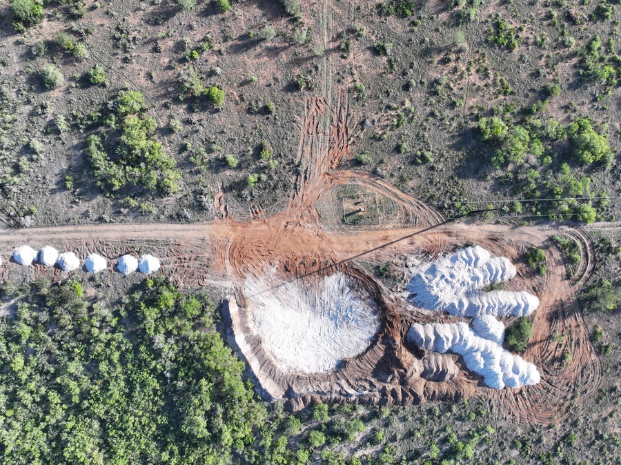 Aerial view of a large-scale land improvement and excavation project, with heavy machinery tracks, exposed soil, and surrounding green vegetation.