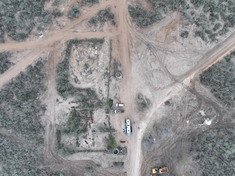 Aerial view of a construction site in a rural area, with various equipment and vehicles visible on the dirt and gravel terrain.