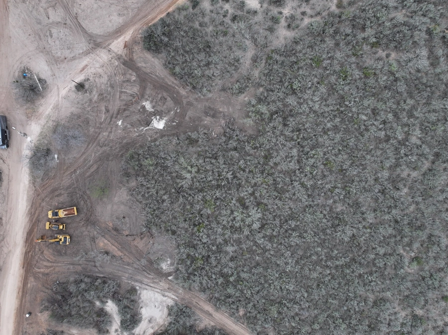 Aerial view of a construction site with heavy machinery and equipment working on a land improvement project in a rural, wooded area.