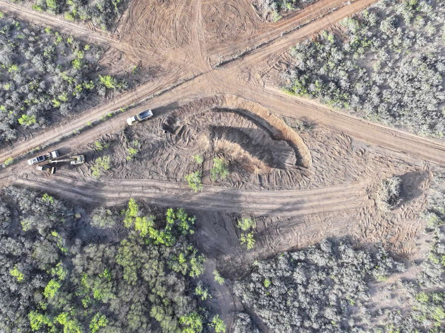Aerial view of a construction site in a forested area, showing heavy machinery and dirt roads winding through the landscape.