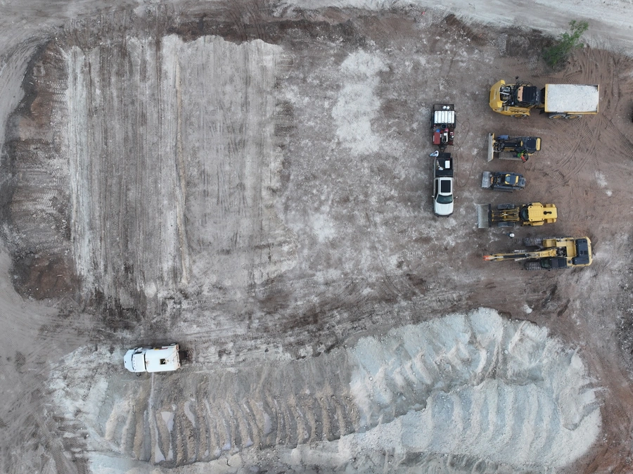Aerial view of a construction site with various heavy machinery and vehicles, including excavators, trucks, and other equipment, on a snowy or icy landscape.
