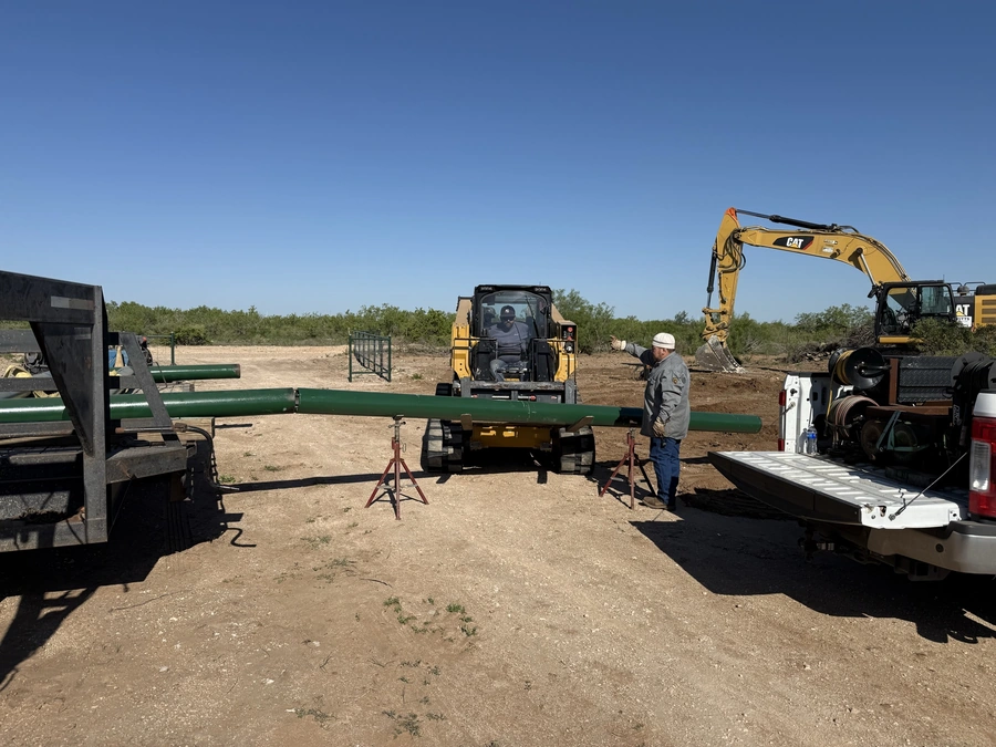 A construction site with excavators, pipes, and a worker inspecting the equipment. The scene shows the early stages of a land improvement or construction project in a rural, natural environment.