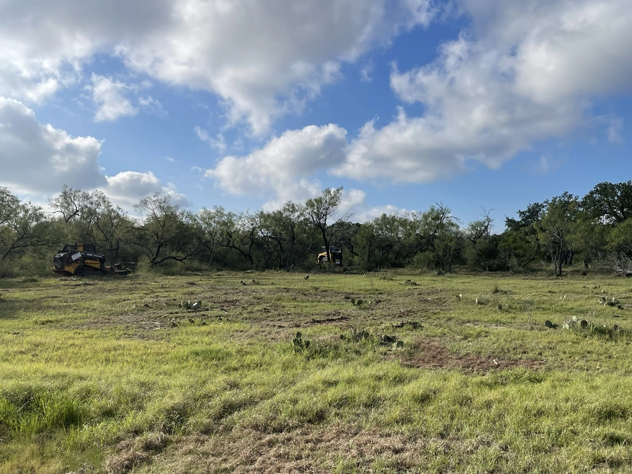 A picturesque rural landscape with heavy machinery and construction equipment in the foreground, surrounded by lush green vegetation and a cloudy blue sky.