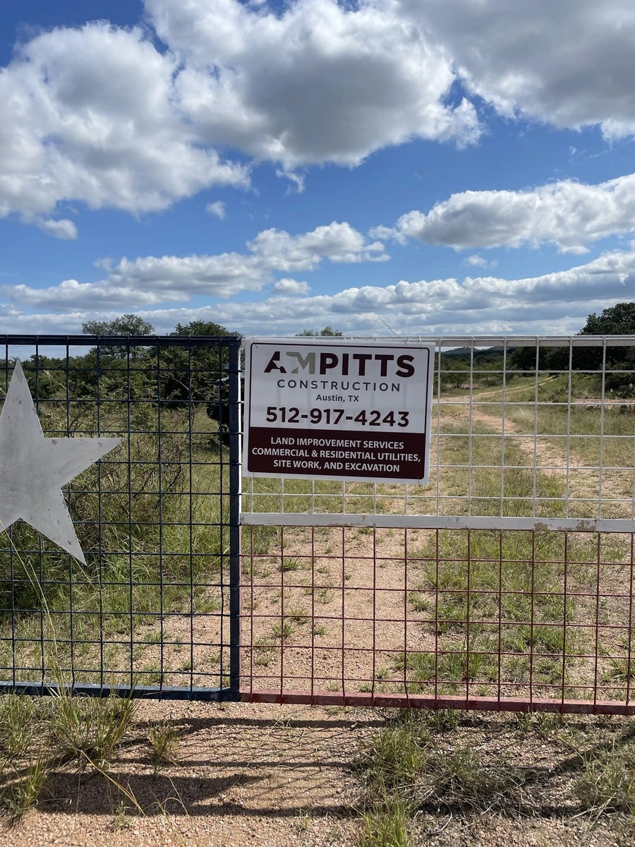 A large construction sign for A.M. Pitts Construction located in Austin, Texas. The sign displays the company's name, contact information, and the services they offer including land improvement, commercial and residential utilities, site work, and excavation.