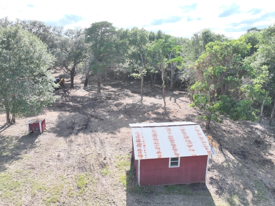A remote, forested area with a small red shed or structure in the foreground. The landscape is rugged with a dirt path winding through the trees.