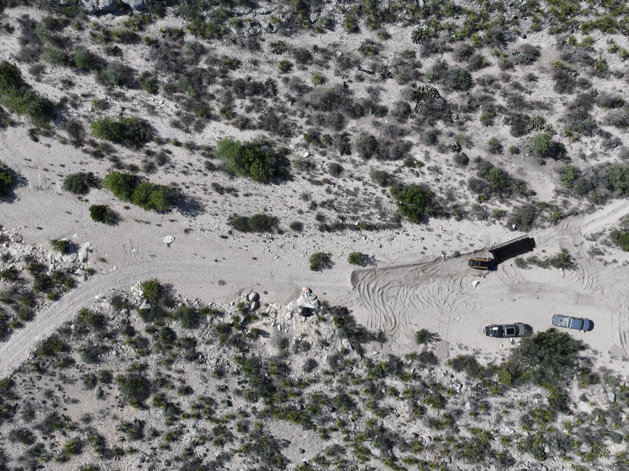 Aerial view of a remote desert landscape with a dirt road, construction vehicles, and sparse vegetation.