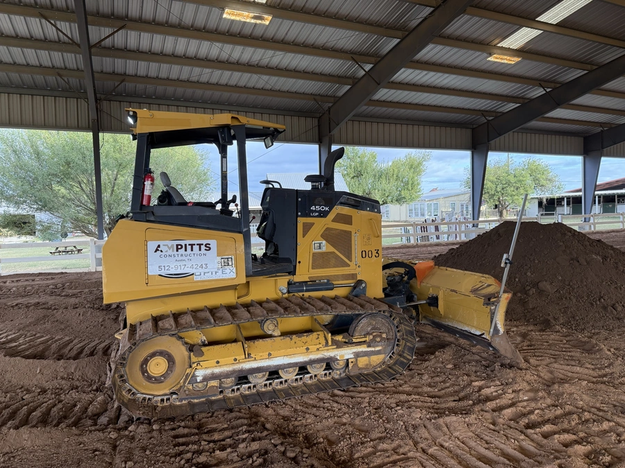 A yellow tracked bulldozer belonging to A.M. Pitts Construction, a construction company that offers land improvement, excavation, and utility services in Central Texas. The bulldozer is working on a construction site, digging into the soil.