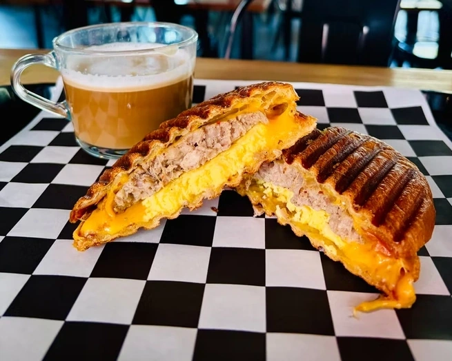 The Blanco Feed Store breakfast panini with sausage, egg, and cheese, cut in half with a coffee.