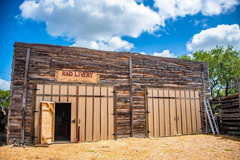 An old wooden building with a "Post Office" sign, surrounded by trees and a blue cloudy sky.