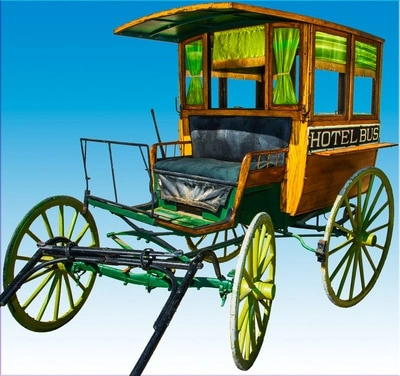 A vintage wooden horse-drawn carriage or wagon painted in bright yellow and green colors. It appears to be an old-fashioned hotel shuttle or bus, with the words "HOTEL BUS" painted on the side.