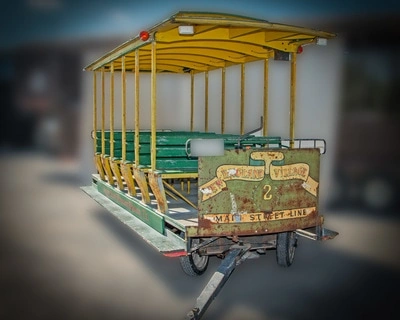 A yellow trolley or tram car with green seats and a bench inside, on a blurred background.