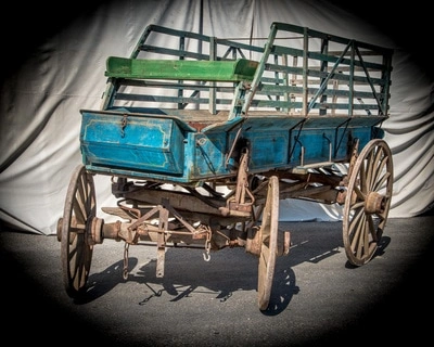 An old, weathered wagon with a wooden frame and blue sides sitting on wooden wheels, bathed in dramatic lighting.