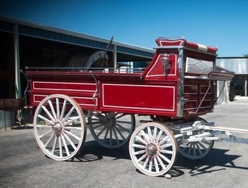 A bright red antique stagecoach wagon with wooden wheels and seats, parked outdoors on a sunny day.