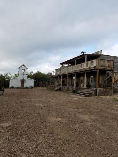 A Western-style town with a church, wooden buildings, and a dusty dirt road in the foreground.