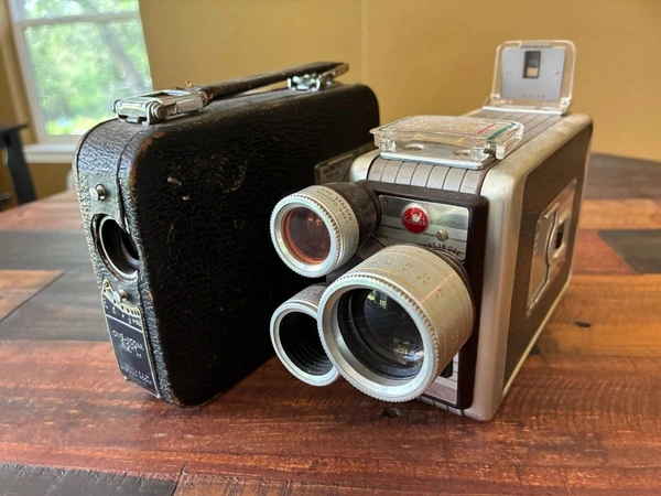 Two vintage cameras-an old black leatherette box camera and a silver twin-lens movie camera-rest on a wooden table, highlighting collectible photography gear ideal for estate sale listings and consignment through Burgess Estate Sales.