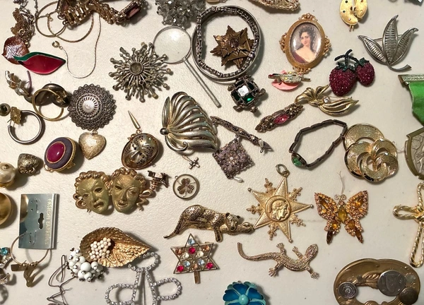 A dense lay-flat collection of vintage and costume jewelry spread across a light surface, featuring brooches, rings, bracelets, necklaces, pendants, earrings, and a cameo portrait. This estate-sale inventory image from Burgess Estate Sales in Central Texas highlights antiques and collectible accessories typical of local estate liquidations in the Austin area.