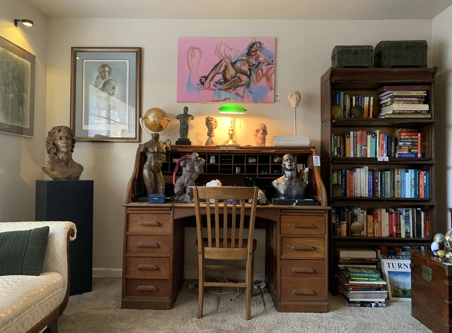 Artistic study featuring vintage roll-top desk, classical sculptures, and art collection