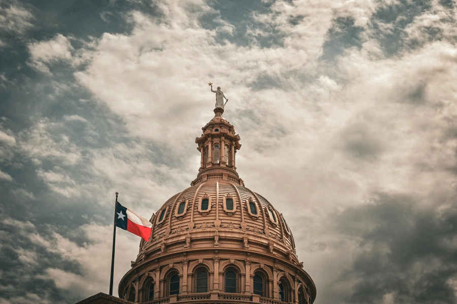 Majestic Texas State Capitol dome with Texas flag flying against dramatic cloudy sky