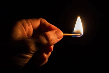 Someone's hand holding a lighted match in the dark