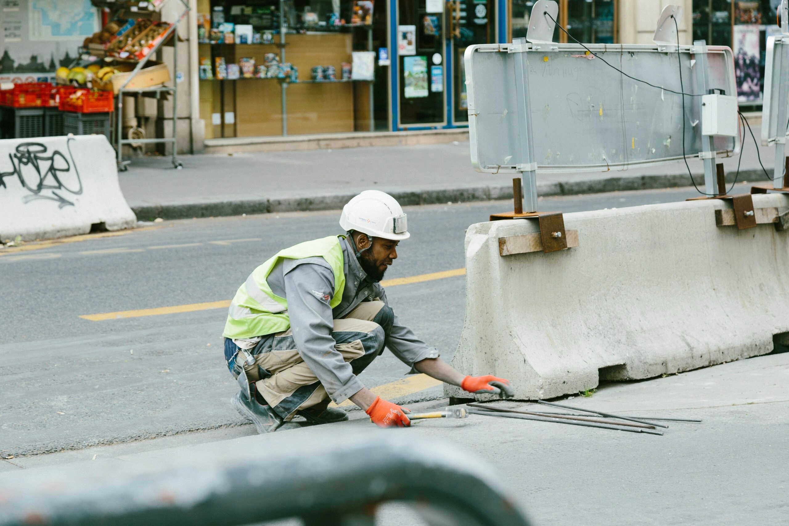 A construction worker in a reflective vest and hard hat is crouched down on the street, working on a construction project.