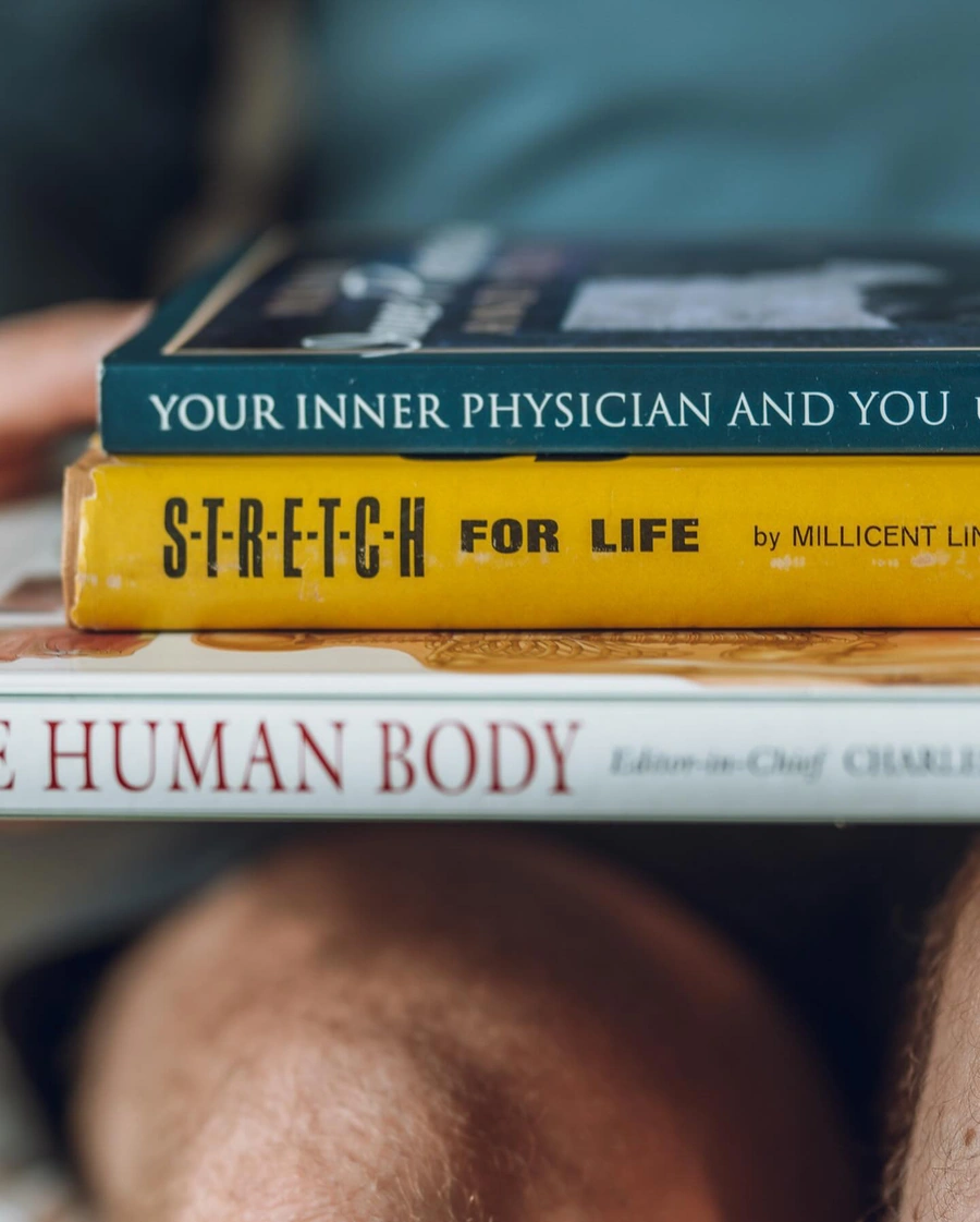 A stack of three books: "Your Inner Physician and You", "Stretch for Life", and "The Human Body". The books are focused on health, wellness, and the human body.