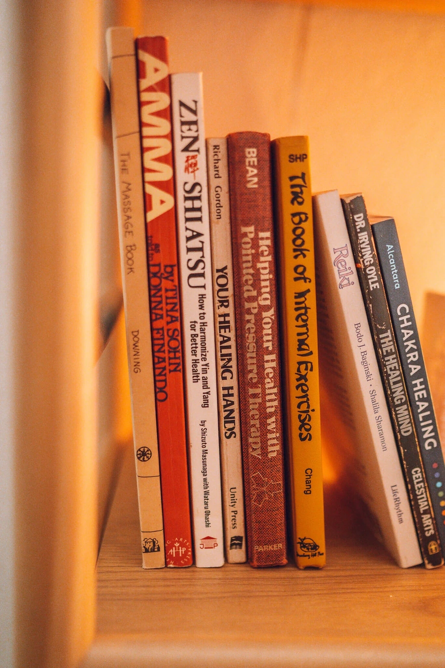 A close-up image of a bookshelf displaying various books related to massage therapy, self-help, and personal growth.
