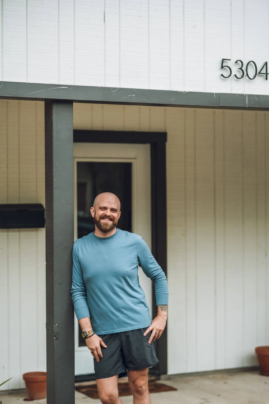 A smiling man with a beard and long hair standing in the doorway of a building with the number 5304 on it.