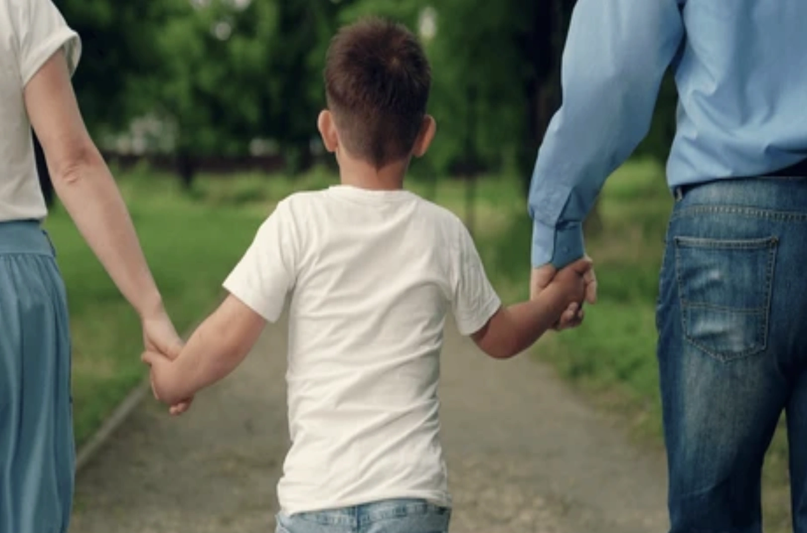 Parents holding hands with little boy walking down park path