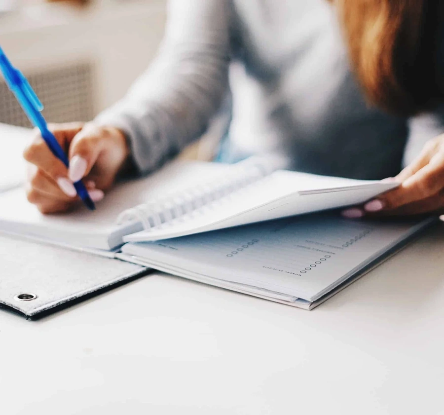 Person writing in a spiral notebook amid legal papers and a binder on an office desk
