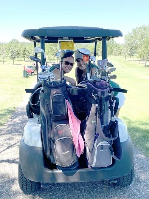 Two people smiling in a golf cart with golf bags on a golf course