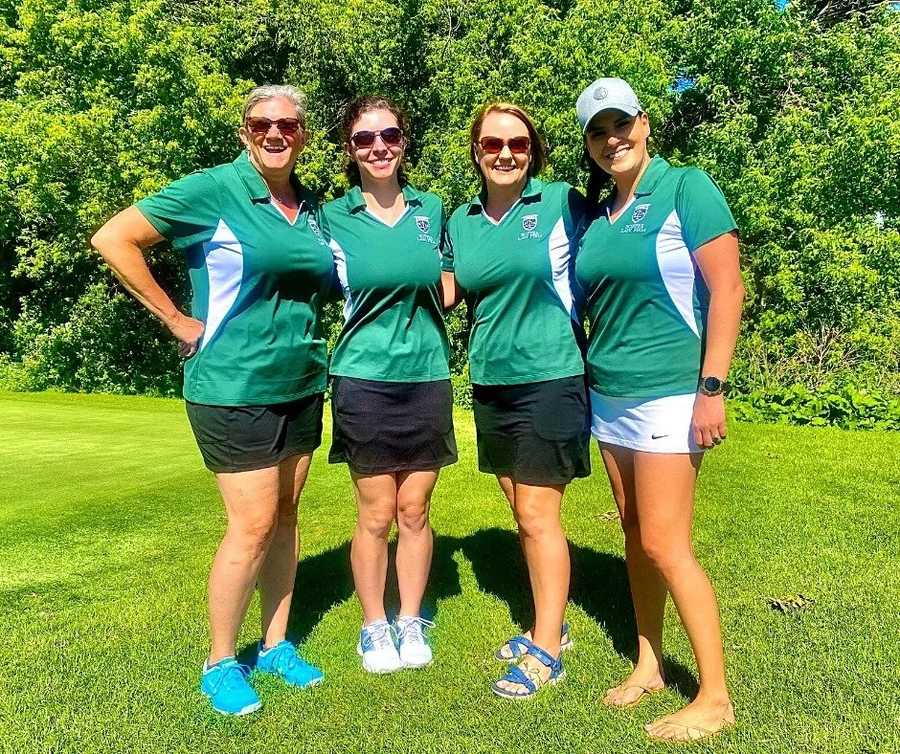 Four women in matching green polo shirts at a community golf event, representing firm volunteer participation.