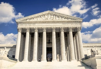 Front facade of a neoclassical courthouse with columns, pediment reliefs, and wide entrance steps against a blue sky