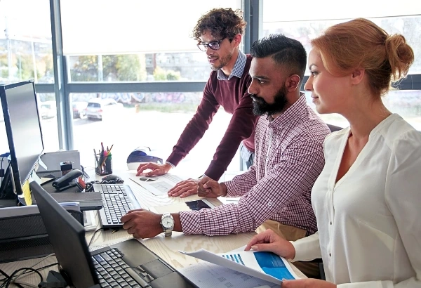 Lawyers collaborating at a desk, reviewing documents and laptop by a bright office window