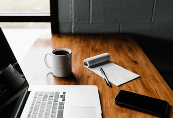 Workspace desk with open laptop, coffee mug, notebook and pen ready for legal research or trademark work