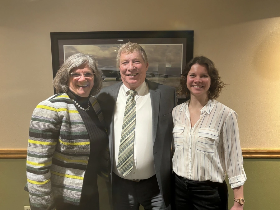 Three people smiling indoors at an honorary commander program event