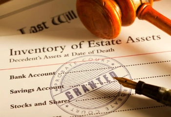Estate inventory and Last Will on a desk with a gavel, fountain pen, and a 'GRANTED' stamp.