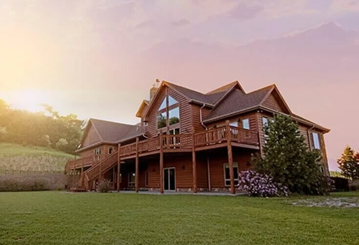 Two-story house with large elevated deck and lawn at sunset, illustrating residential property.